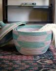 Woven basket with a patterned lid on a decorative rug, with a shelf in the background.
