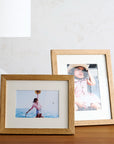 Two wooden picture frames with photos of people on a table against a white wall.