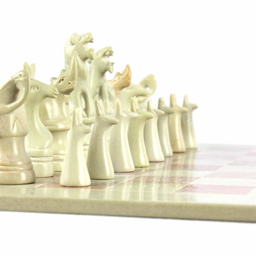 A hand-carved soapstone chess set with a green and pink checkered board and beige, pink, and white stone pieces zoomed in on the white pieces.