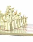 A hand-carved soapstone chess set with a green and pink checkered board and beige, pink, and white stone pieces zoomed in on the white pieces.