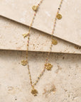 Gold necklaces with floral pendants on a textured beige surface