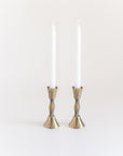 A pair of hand-forged iron candle holders with a brass finish holding candles and featuring a textured design.