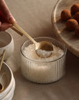 A hand holding a spoon with a loop handle scooping salt