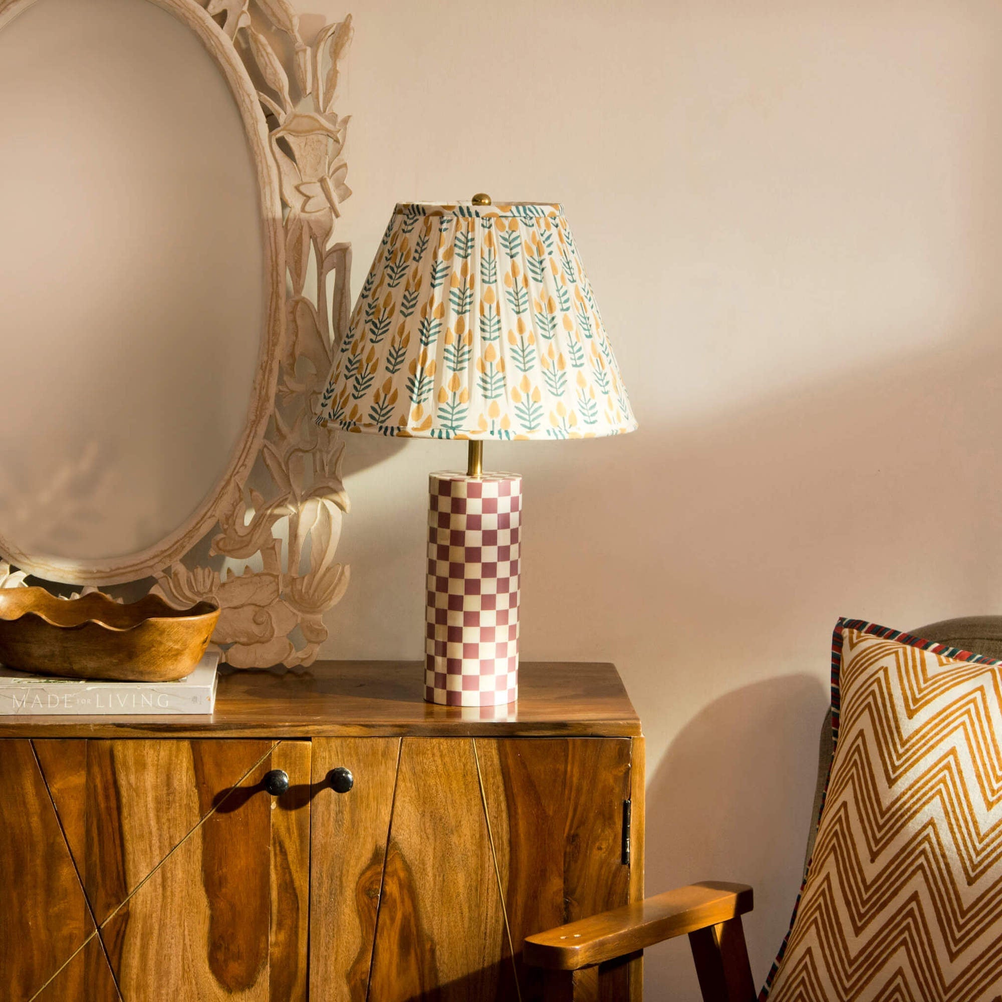 Decorative lamp with patterned shade on a wooden surface next to a mirror and chair.