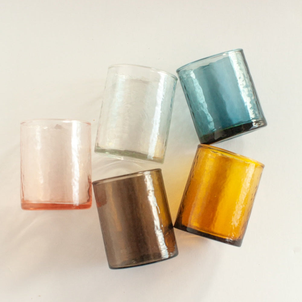 A collection of five handblown glasses with a hammered finish, displayed in clear, blue, brown, clear and yellow colors