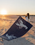 A pair of lobster-shaped rugs in white on a beach being placed on sand on the beach
