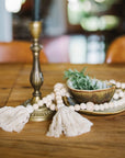 Decorative items on a wooden table including a brass candlestick, beads, and a small bowl with greenery