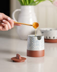 Person pouring honey into a ceramic container with a cracked glaze design.