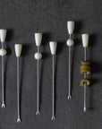 Set of metal cocktail picks with white ceramic ends on a dark background
