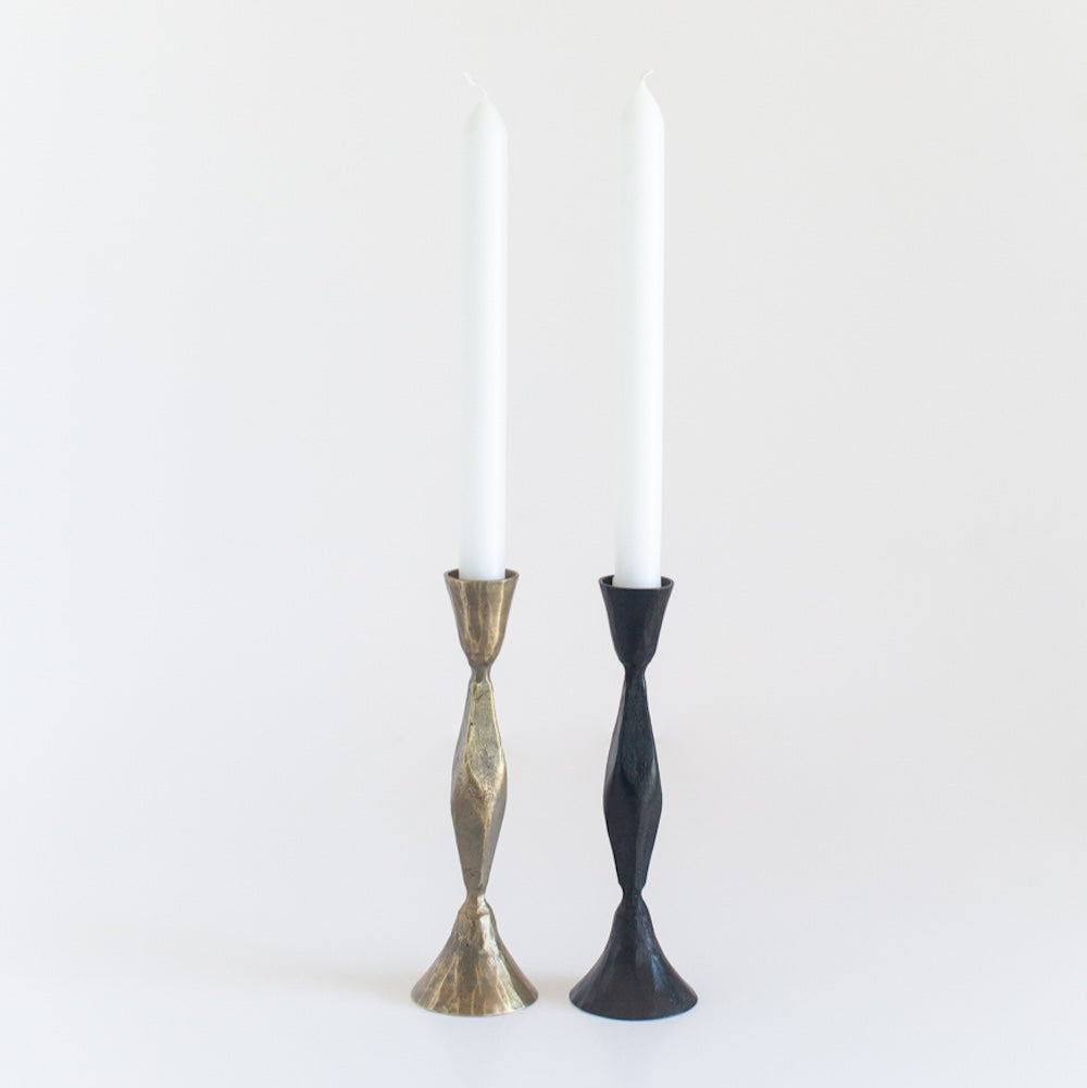 Two candlesticks, one gold and one black, holding white candles on a white background