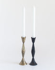 Two candlesticks, one gold and one black, holding white candles on a white background