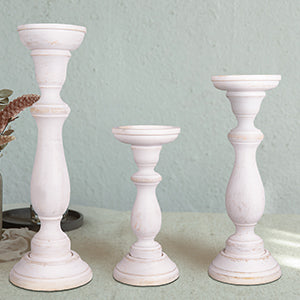 A set of three white shabby chic wooden candleholders in varying sizes on a table with a green background
