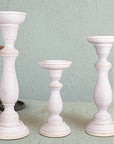 A set of three white shabby chic wooden candleholders in varying sizes on a table with a green background