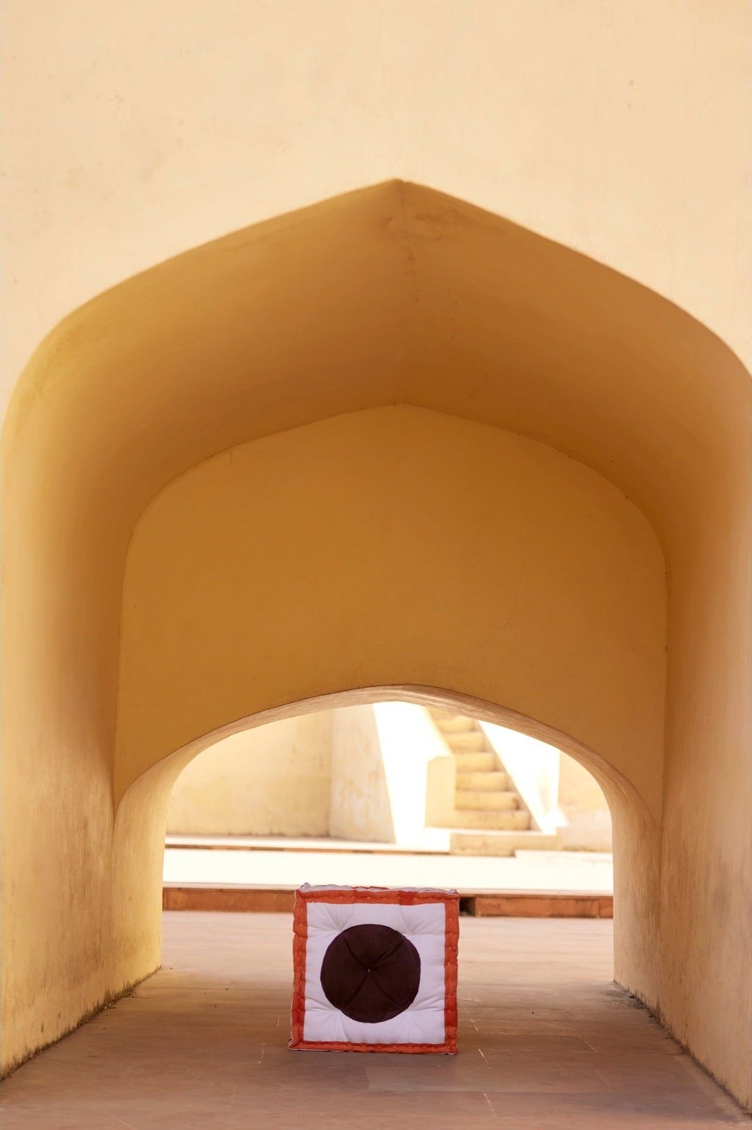 Decorative floor cushion with geometric pattern on a stone floor, framed by beige arches