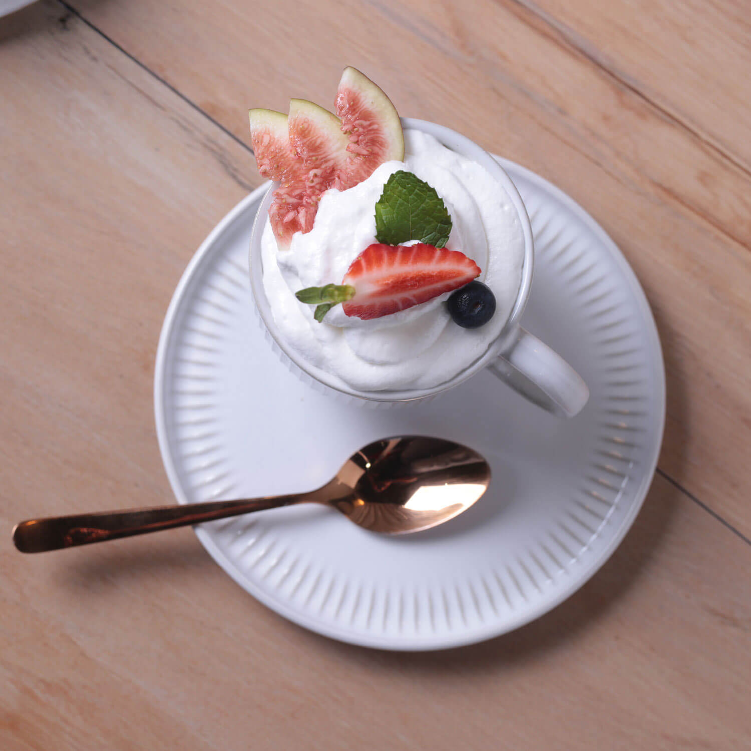Cup of dessert with whipped cream, fruit, and a spoon on a wooden table