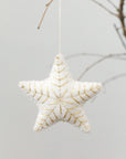 Star-shaped decorative ornament with gold embroidery on a branch against a light background