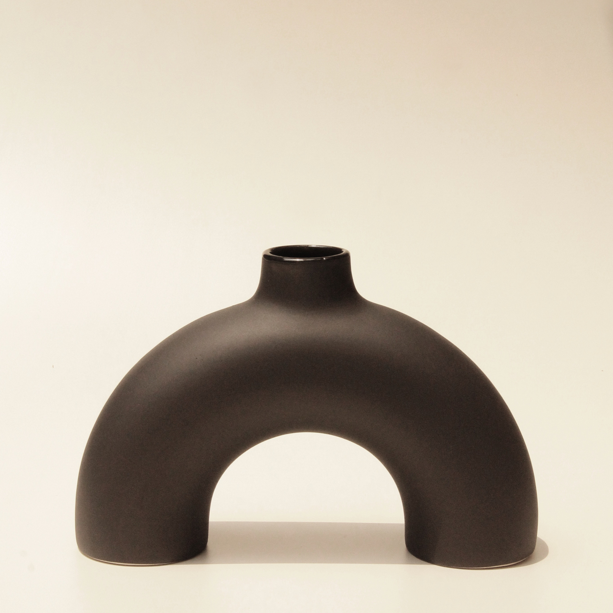A black, arch-shaped ceramic vase with a smooth finish