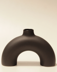A black, arch-shaped ceramic vase with a smooth finish