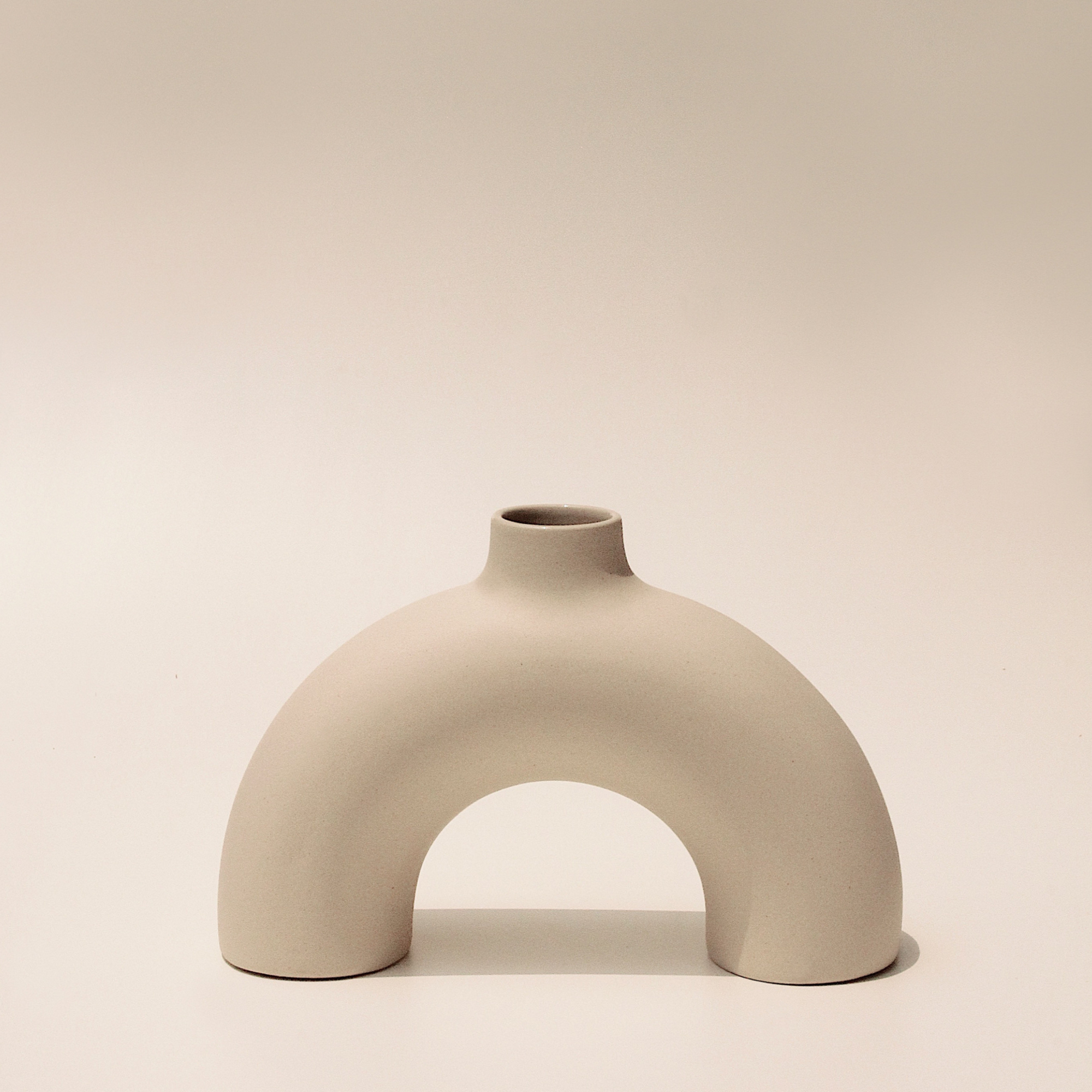 A beige, arch-shaped ceramic vase with a smooth finish