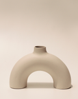 A beige, arch-shaped ceramic vase with a smooth finish