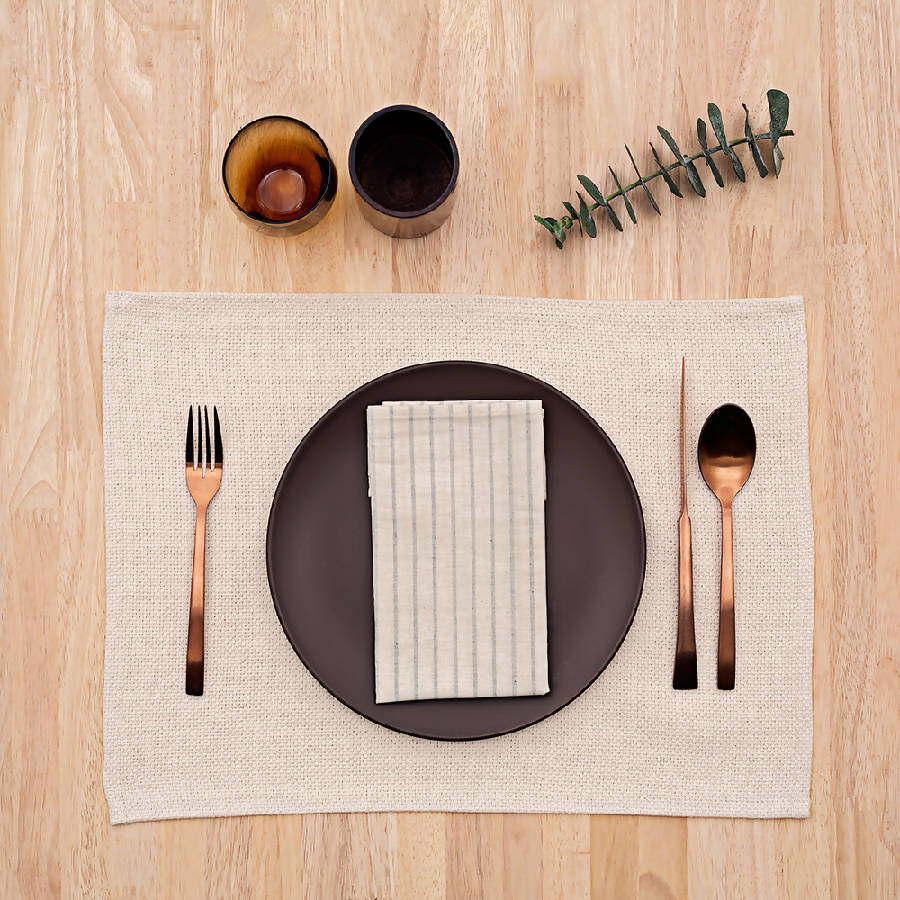 A beige rustic placemat with utensils, a plate and a napkin on top