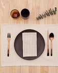 A beige rustic placemat with utensils, a plate and a napkin on top