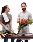 Two people wearing aprons. One is wearing a striped crossback bib apron with multiple pockets and a utility loop. The other is wearing a waist apron.