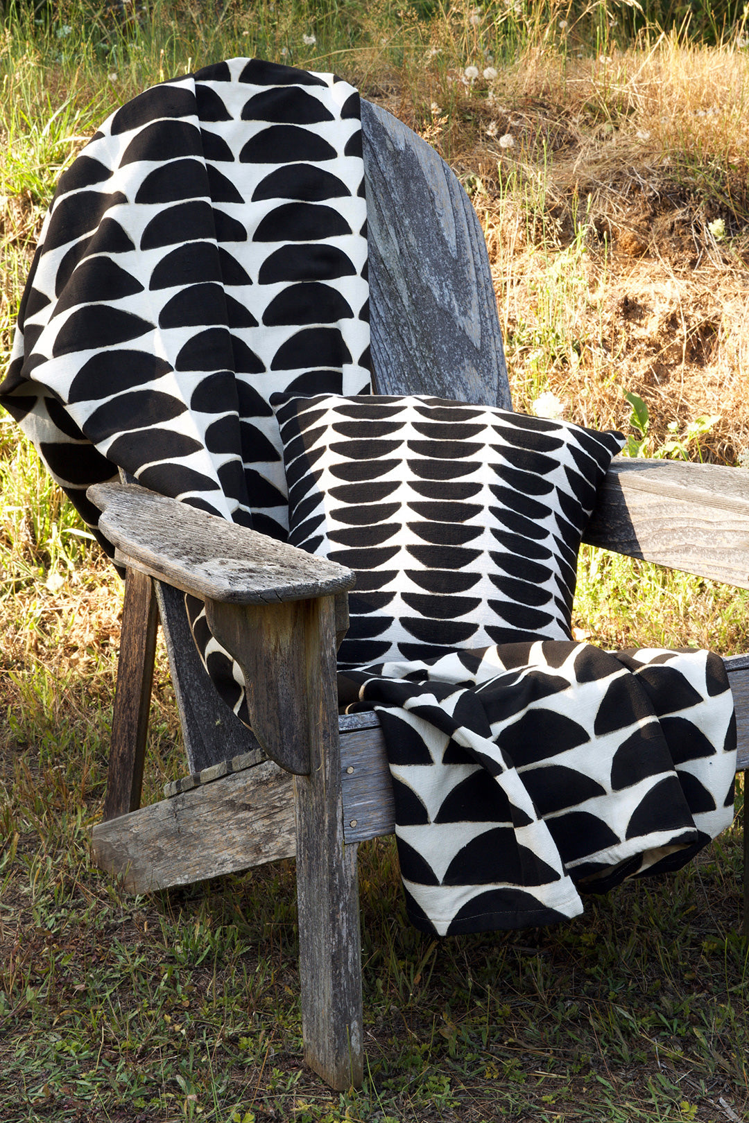 A black and white throw blanket folded over a wooden chair outside