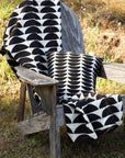 A black and white throw blanket folded over a wooden chair outside