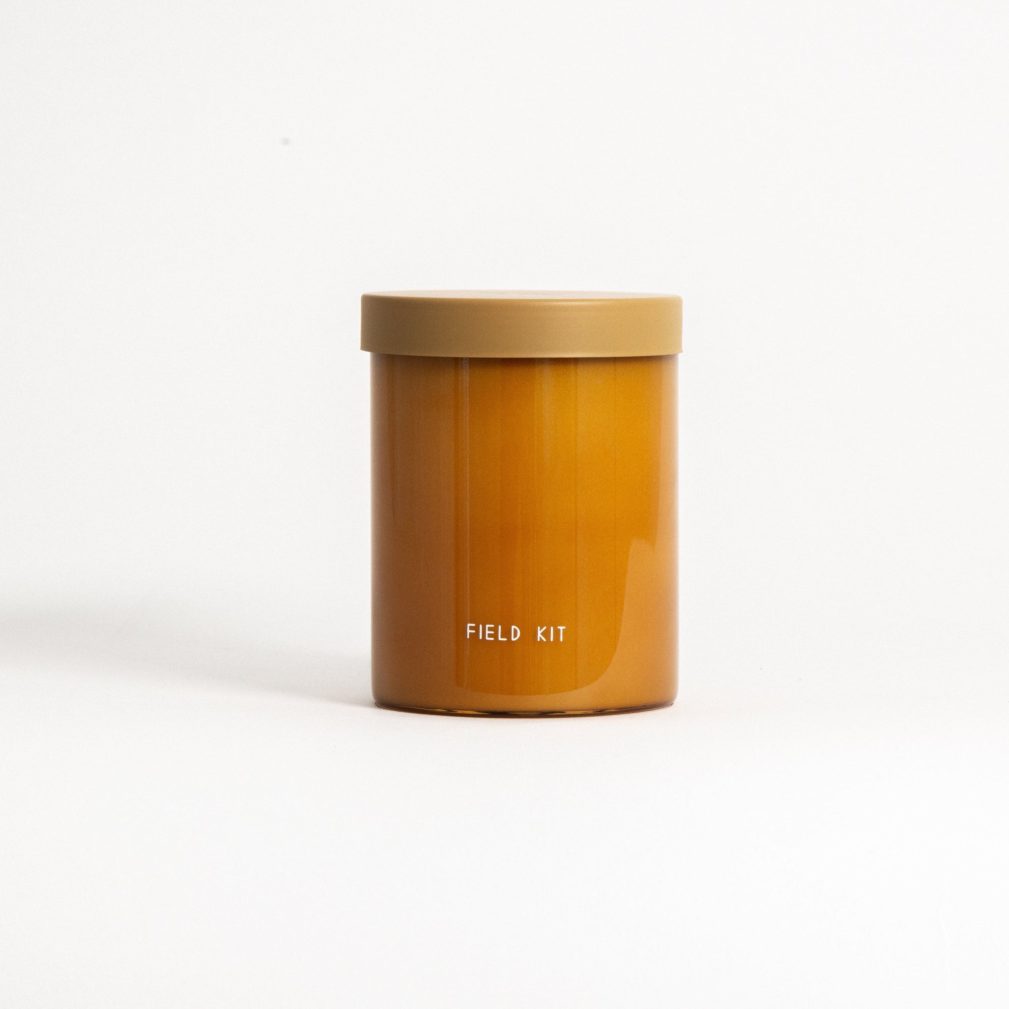 A brown cylindrical soy wax candle in a reusable glass jar with a lid, labeled 'FIELD KIT'.