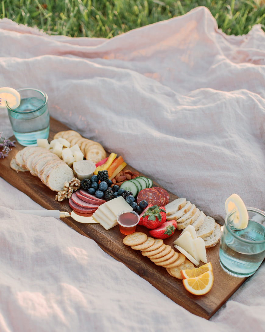 Charcuterie board with snacks and drinks on a picnic blanket