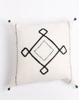 A square-shaped throw pillow with a beige background and black geometric embroidery design, featuring small tassels on the corners
