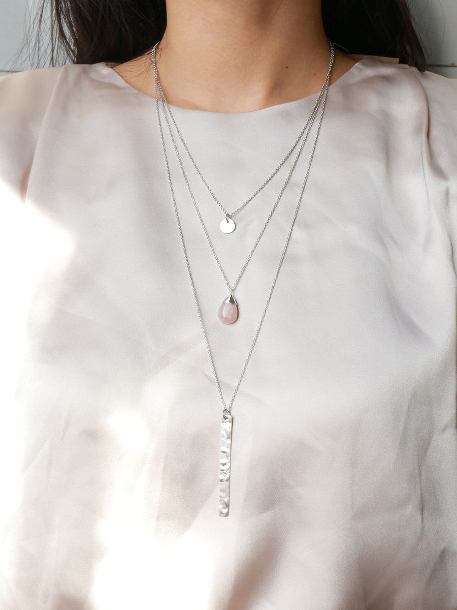 A silver multi-strand multi-way pendant necklace with a pink chalcedony centerpiece stone on a model's neck.