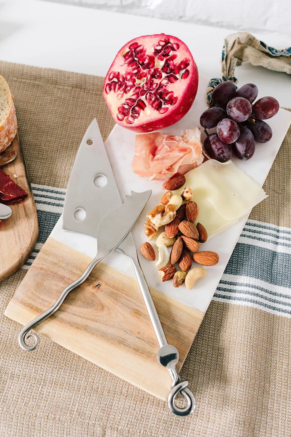 Wooden cutting board with cheese, fruits, and nuts on a striped fabric background