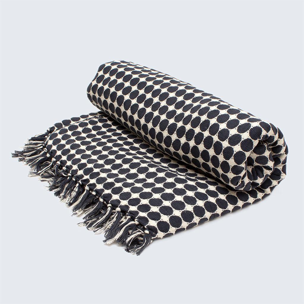 A folded handwoven throw with black circles on a white background, featuring a fringe edge