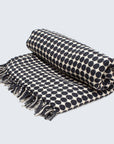 A folded handwoven throw with black circles on a white background, featuring a fringe edge