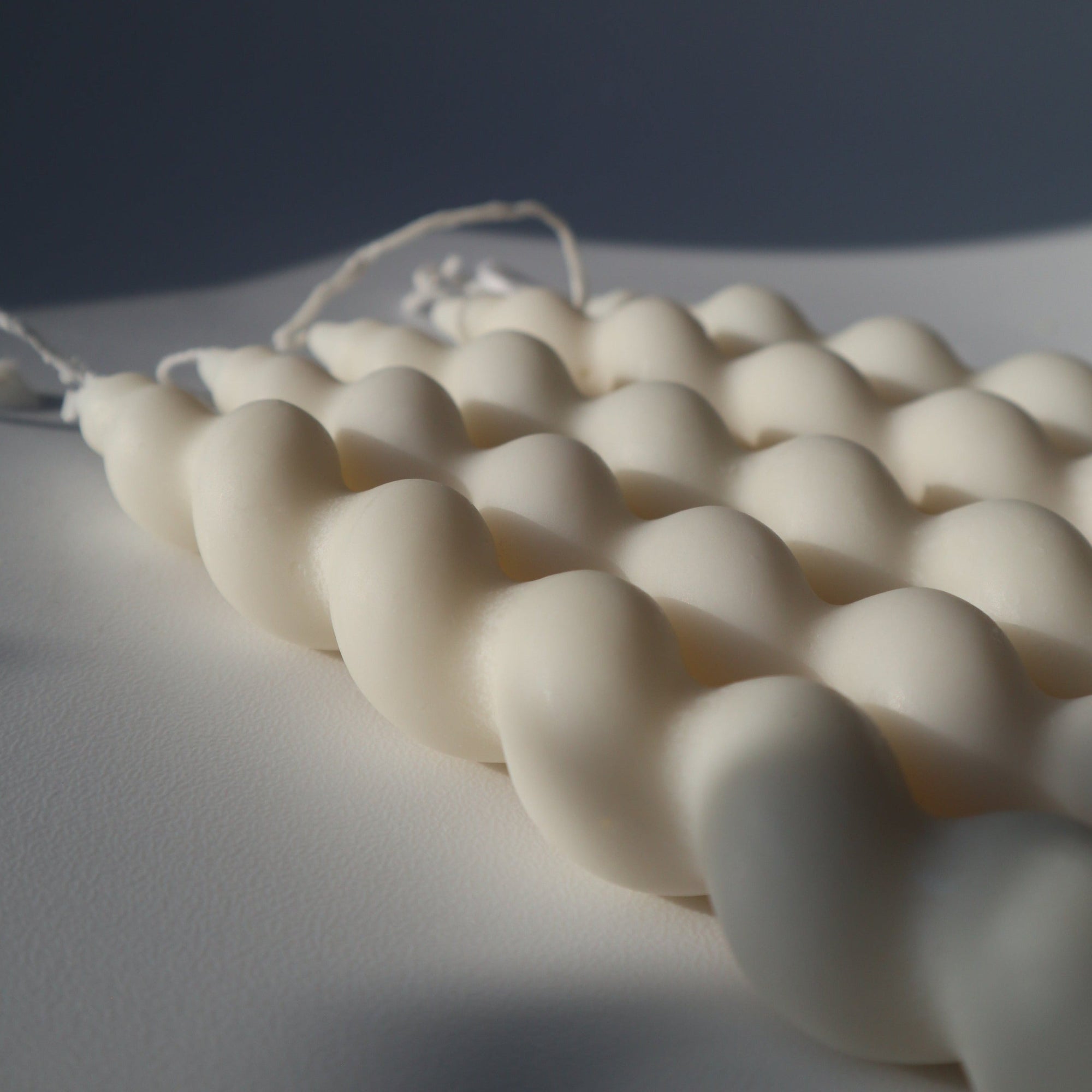 A close-up image of a white, twisted taper candle made of soy wax, showing its textured and twisted design.