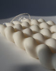 A close-up image of a white, twisted taper candle made of soy wax, showing its textured and twisted design.