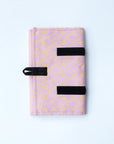 A jewelry roll travel case with various compartments for earrings, rings, and necklaces, displayed alongside some jewelry items and a patterned fabric with a geometric design in pink and yellow.