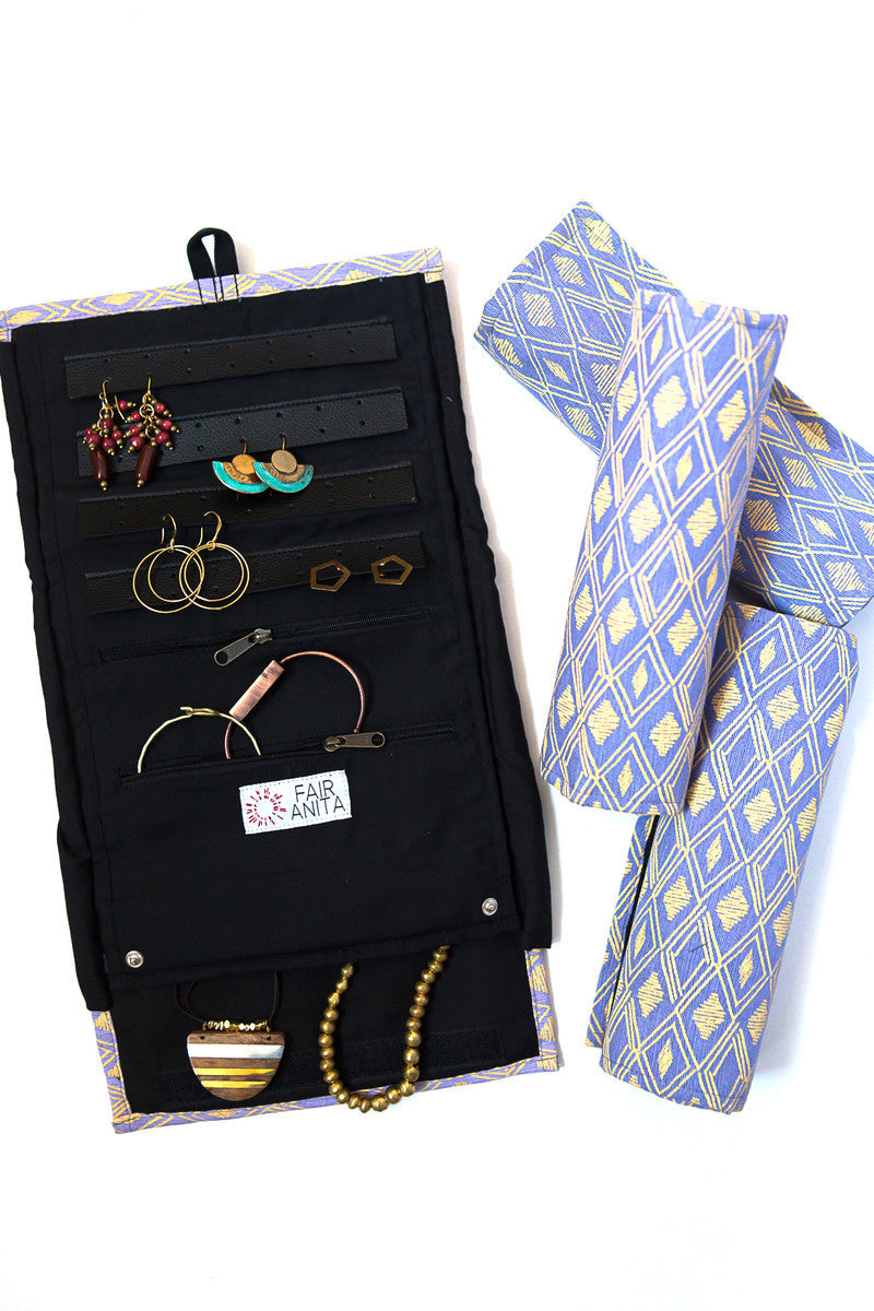 A jewelry roll travel case with various compartments for earrings, rings, and necklaces, displayed alongside some jewelry items and a geometric blue and yellow patterned fabric.