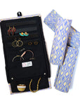 A jewelry roll travel case with various compartments for earrings, rings, and necklaces, displayed alongside some jewelry items and a geometric blue and yellow patterned fabric.