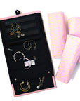 A jewelry roll travel case with various compartments for earrings, rings, and necklaces, displayed alongside some jewelry items and a patterned fabric in pink.