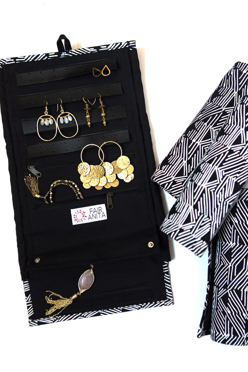 A jewelry roll travel case in a black matchstick design, unrolled to display compartments for earrings, rings, and necklaces, with the case's fabric 'wings' folded over the top layer to protect the jewelry.
