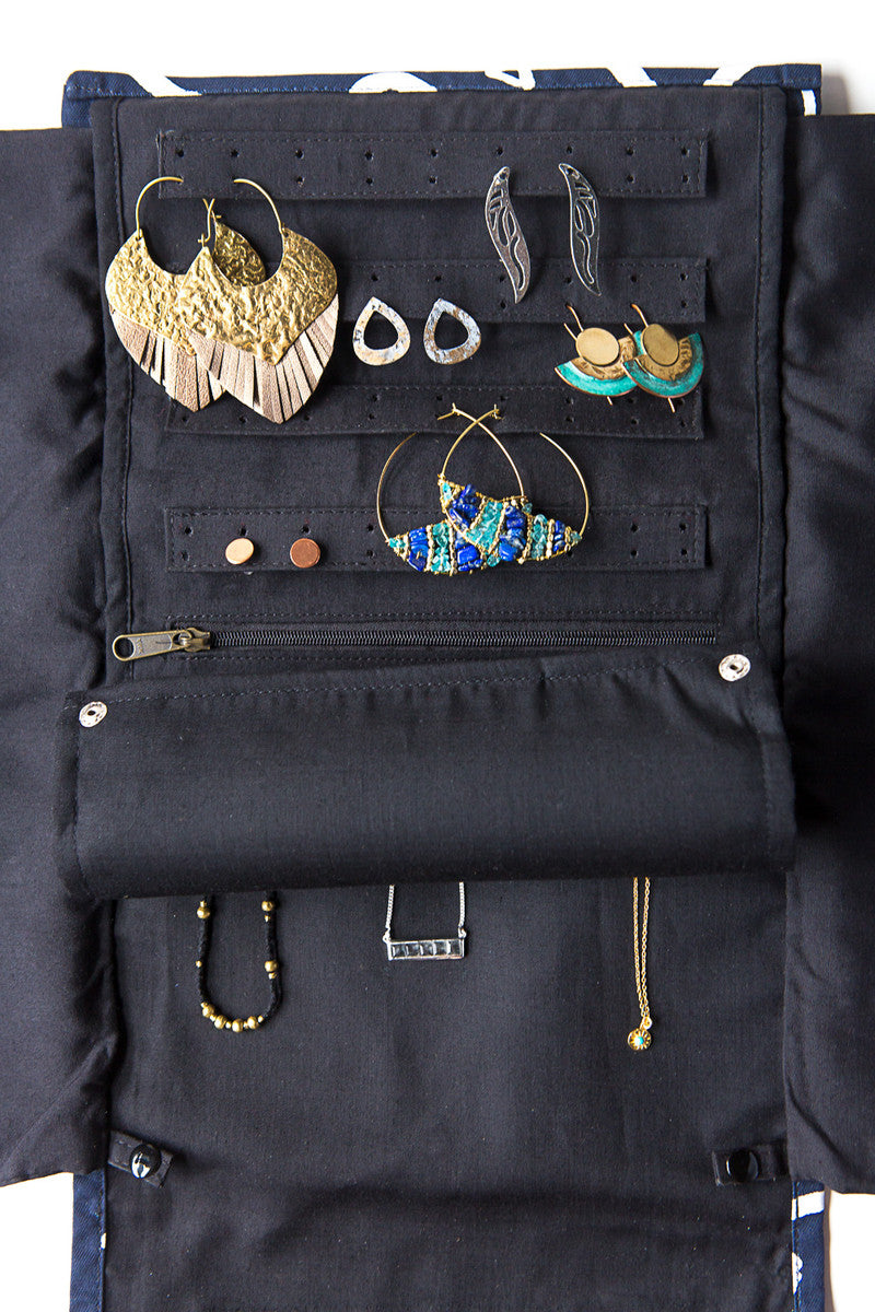 A jewelry roll travel case in a black matchstick design, unrolled to display compartments for earrings, rings, and necklaces with jewelry inside.