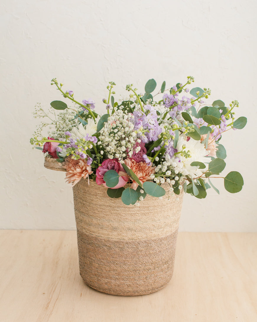 Floral arrangement in a woven basket on a wooden surface.