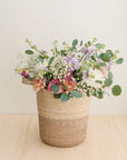 Floral arrangement in a woven basket on a wooden surface.