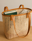 Woven bag with leather handles and trim on a wooden surface