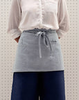 A person wearing a gray waist apron with multiple pockets and a utility loop