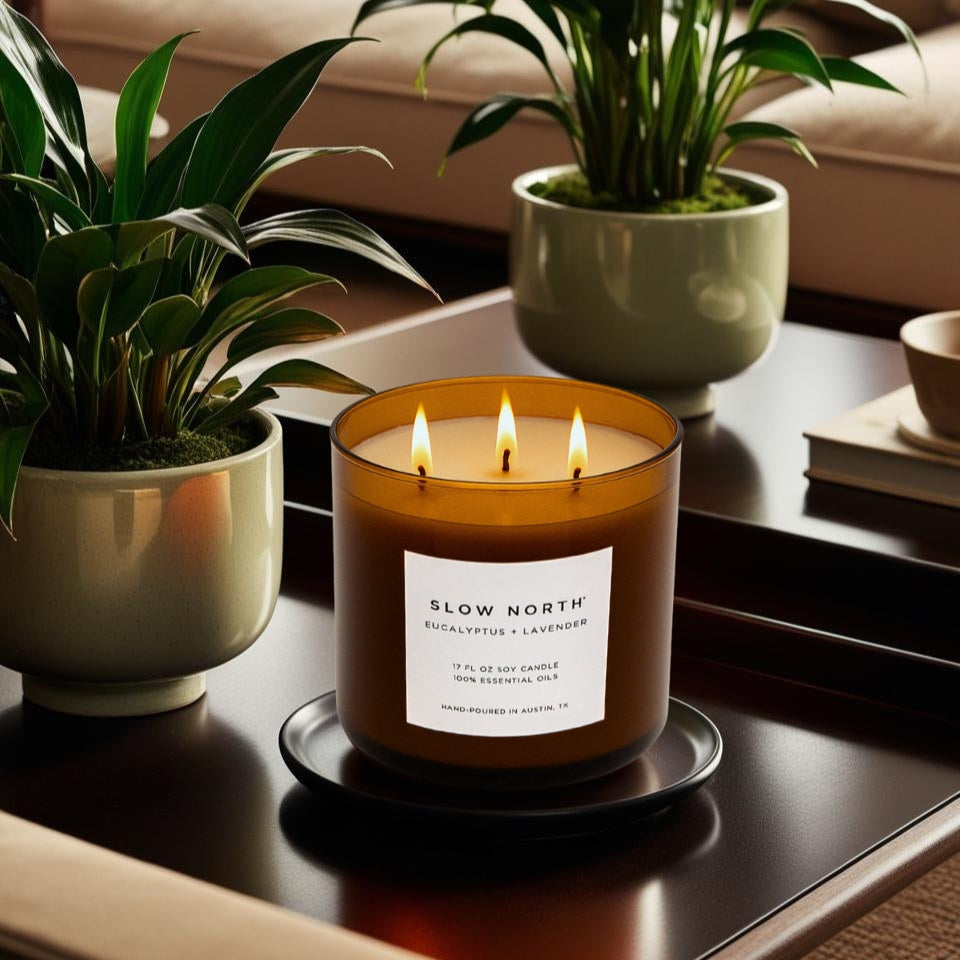 Candle with 'Slow North' label on a table with plants and books