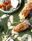 Baguette slices on a floral-patterned tablecloth with cherry tomatoes and a small plate in the background.